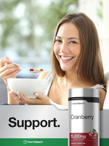 Young woman smiling while eating cereal with a Horbäach Cranberry supplement bottle beside her.