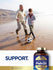 An older man and a young boy play soccer on a beach next to a bottle of Carlyle Fish Oil.