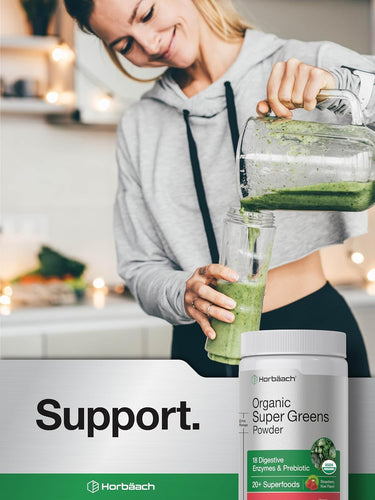 A young woman pours a green smoothie from a blender into a glass, next to a jar of Organic Super Greens Powder.