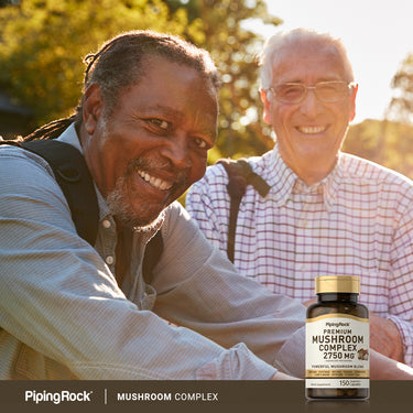 Two elderly men smiling outdoors while holding a Mushroom Complex bottle.