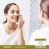 Young woman applies cream to her face next to an Aloe Vera Cream jar, smiling gently.