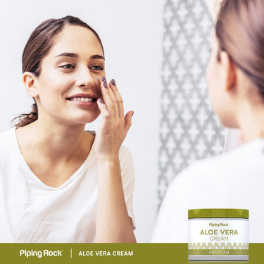 Young woman applies cream to her face next to an Aloe Vera Cream jar, smiling gently.