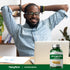 A young adult Black man sits relaxed at a desk next to an Ashwagandha bottle.