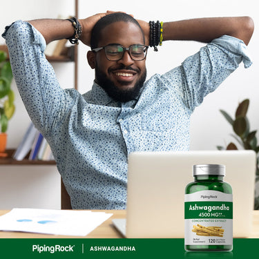 A young adult Black man sits relaxed at a desk next to an Ashwagandha bottle.