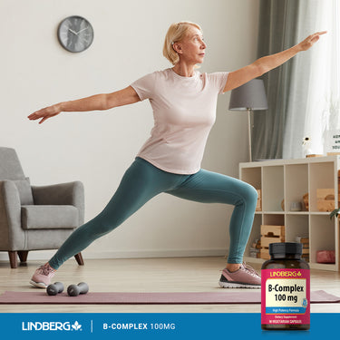 An older woman practices yoga next to a B-Complex bottle, highlighting health and wellness routine.