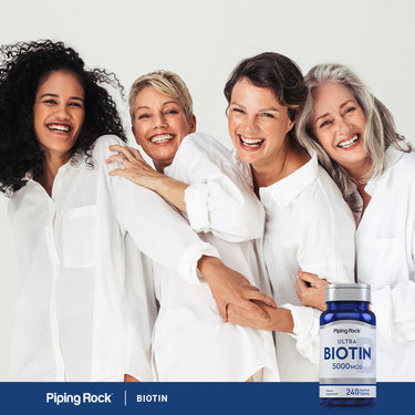Four joyful women of different ages laugh and hug each other near a bottle of Biotin.