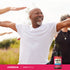 A senior Black man practicing yoga outside with a CoQ10 supplement bottle nearby.