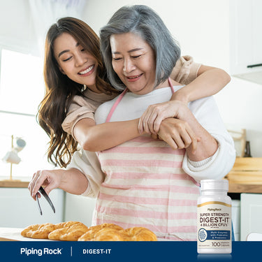 Two Asian women, one young and one older, embrace while baking croissants with a DIGEST-IT bottle close by.