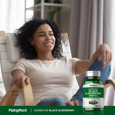 Smiling young woman relaxes in a lounge chair next to an Elderberry bottle.