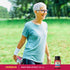 A senior woman stretches her leg in a park near a bottle of Grape Seed Extract.