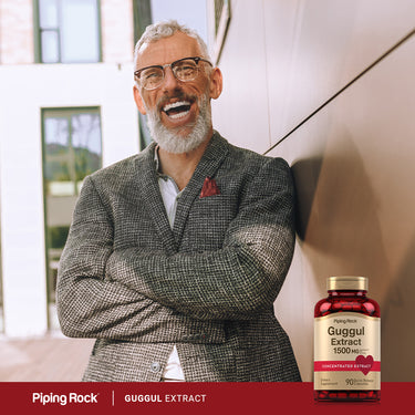 Older man laughing against a wall with a Guggul Extract bottle beside him.