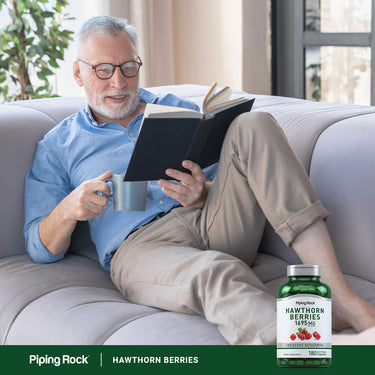 An older man reads a book and sips from a mug next to a bottle of Hawthorn Berries.