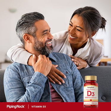A happy couple sitting on a couch, smiling and holding D3 Softgels.