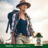 An older woman hiking on a trail, wearing a hat and backpack, with a bottle of Horse Chestnut Extract beside her.