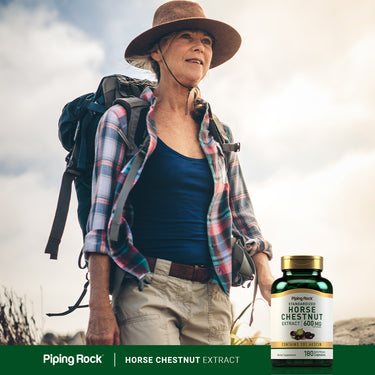 An older woman hiking on a trail, wearing a hat and backpack, with a bottle of Horse Chestnut Extract beside her.