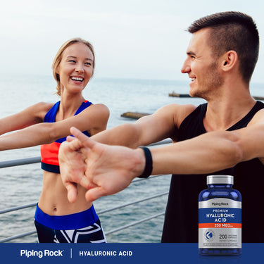 A young man and woman stretch outdoors by the water with a Hyaluronic Acid bottle visible nearby.