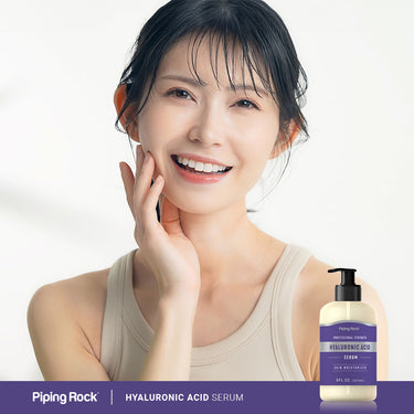 Young woman smiling and touching her cheek next to a Hyaluronic Acid Serum bottle.