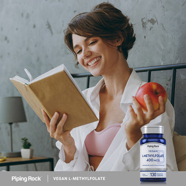 Young adult woman reads a book and holds an apple next to a Vegan L-Methylfolate bottle, depicting a healthy lifestyle.