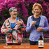 Two older women jogging and laughing outdoors near a Liquid Turmeric + Ginger bottle.