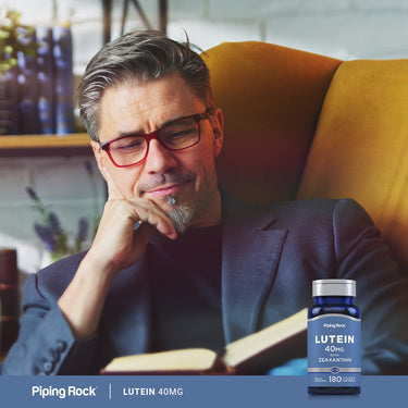 A man with grey hair and glasses is reading a book next to a Lutein + Zeaxanthin supplement bottle.