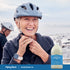 Senior woman smiling and adjusting a bicycle helmet, with a man in the background, next to a Magnesium Oil bottle.