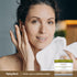 Woman touching her face with a towel, next to a jar of Royal Jelly & Manuka Honey Cream.