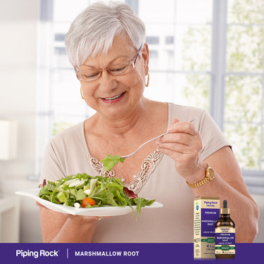 An older woman eating a salad with a bottle and box of Marshmallow Root Liquid Extract beside her.
