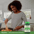 Young woman cooks in a kitchen near a Whole Greens supplement bottle.
