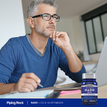 Middle-aged man thinking at a desk with a laptop and notebook, next to a bottle of NADH + Co Q-10 Optimizer.