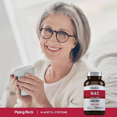 An older woman smiles while holding a mug, with a bottle of NAC next to her.