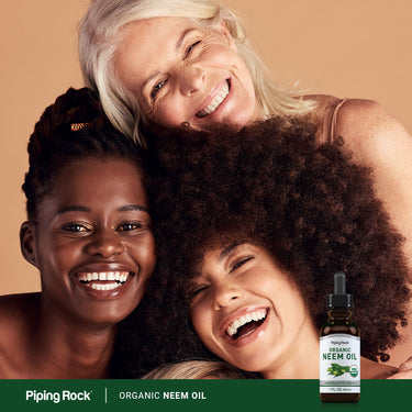 Three diverse women, happy and embracing, holding a bottle of Organic Neem Oil.