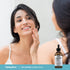 Young woman smiling, touching her cheek in a mirror, next to a Niacinamide & Zinc Serum bottle.