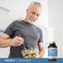 An elderly man prepares a salad next to a bottle of Fish Oil Lemon Softgels, promoting healthy lifestyle choices.