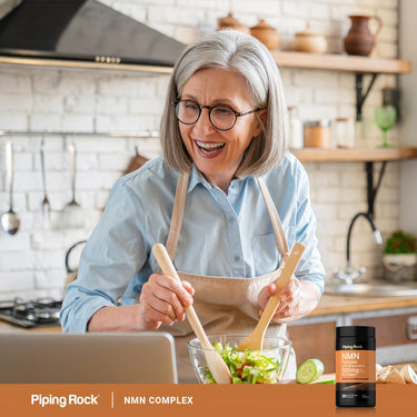 Adult preparing a salad in a kitchen with a Piping Rock NMN Complex with Resveratrol 500 mg & Collagen bottle nearby.