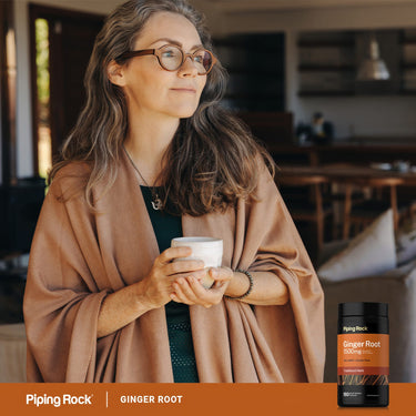 Middle-aged woman with a mug, wearing a shawl, next to a bottle of Ginger Root 1500 mg.