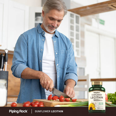 A middle-aged man chops tomatoes in a kitchen, with a bottle of Sunflower Lecithin nearby.