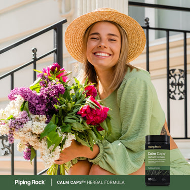 Smiling young woman holds a large bouquet of flowers next to a bottle of Calm Caps.