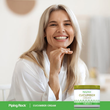 Lifestyle image of a smiling adult with a Piping Rock Cucumber Cream, 4 oz. (113 g), displayed in the bottom right corner