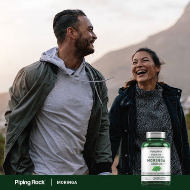 Adults laughing while walking outdoors, holding a bottle of Moringa.