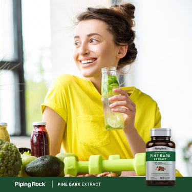 Smiling young woman holding infused water with a Pine Bark Extract bottle on the table in front of her.
