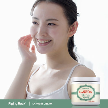 A young woman smiles, touching her cheek next to a jar of Lanolin.