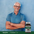 An older man smiling with arms crossed stands beside a bottle of Pycnogenol.