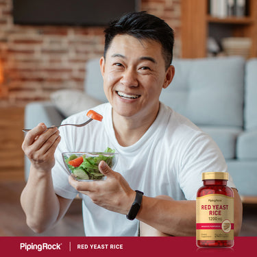 Asian man smiling while holding a salad bowl and fork, with a Red Yeast Rice bottle nearby.