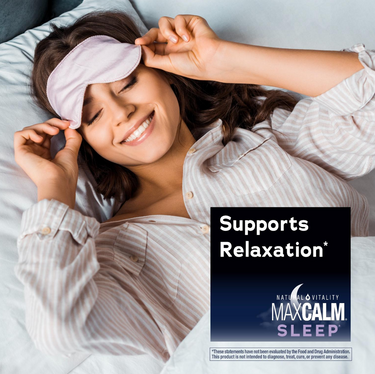 A smiling woman in bed adjusts her sleep mask alongside a graphic for Natural Vitality MaxCalm Sleep, stating 'Supports Relaxation*'.