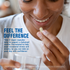 An adult woman smiles while holding an Ashwagandha capsule and a glass of water.
