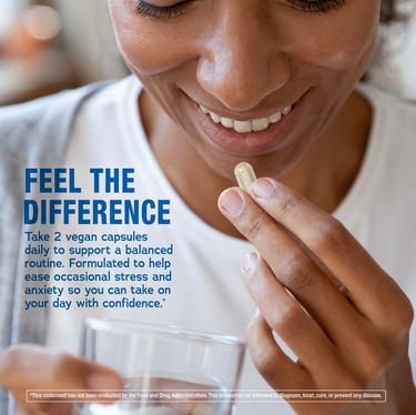An adult woman smiles while holding an Ashwagandha capsule and a glass of water.