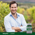 A smiling man in his 30s stands outdoors with arms crossed beside a bottle of Selenium.