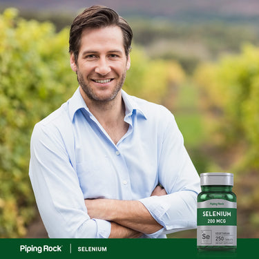 A smiling man in his 30s stands outdoors with arms crossed beside a bottle of Selenium.