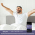 A man stretches in bed after waking up with a Sleep Melatonin Gummies bottle nearby.