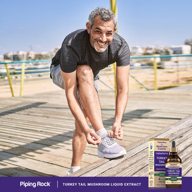 A middle-aged man smiles while lacing his running shoes next to a Turkey Tail Mushroom Liquid Extract bottle.